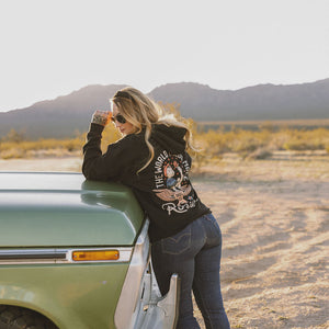 Kendall wearing the black Rosie hoodie and leaning on a truck 